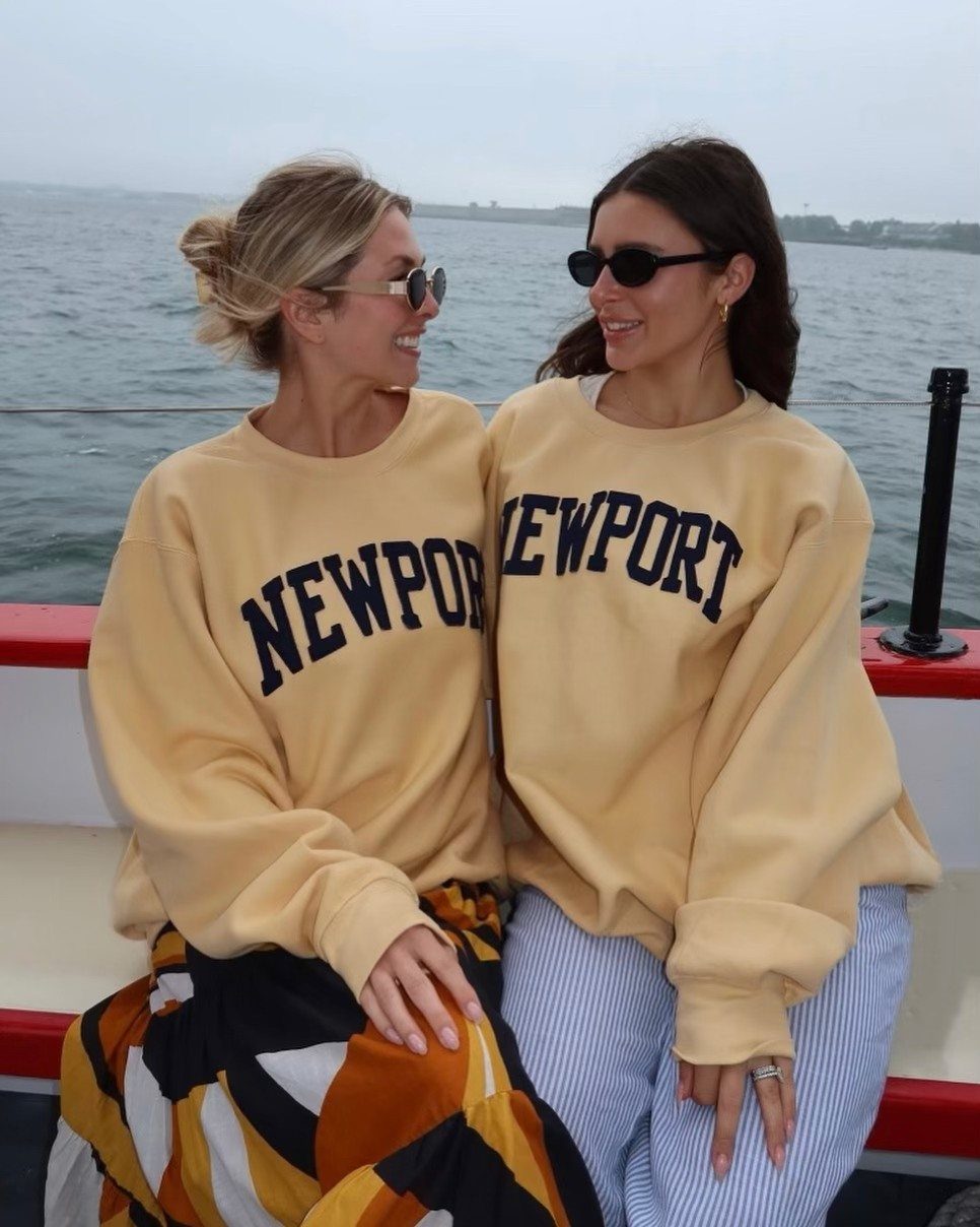 Two women in Newport sweatshirts sitting on a boat on the water.