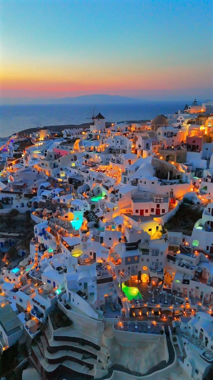 White buildings of a hillside village at sunset with a traditional windmill.