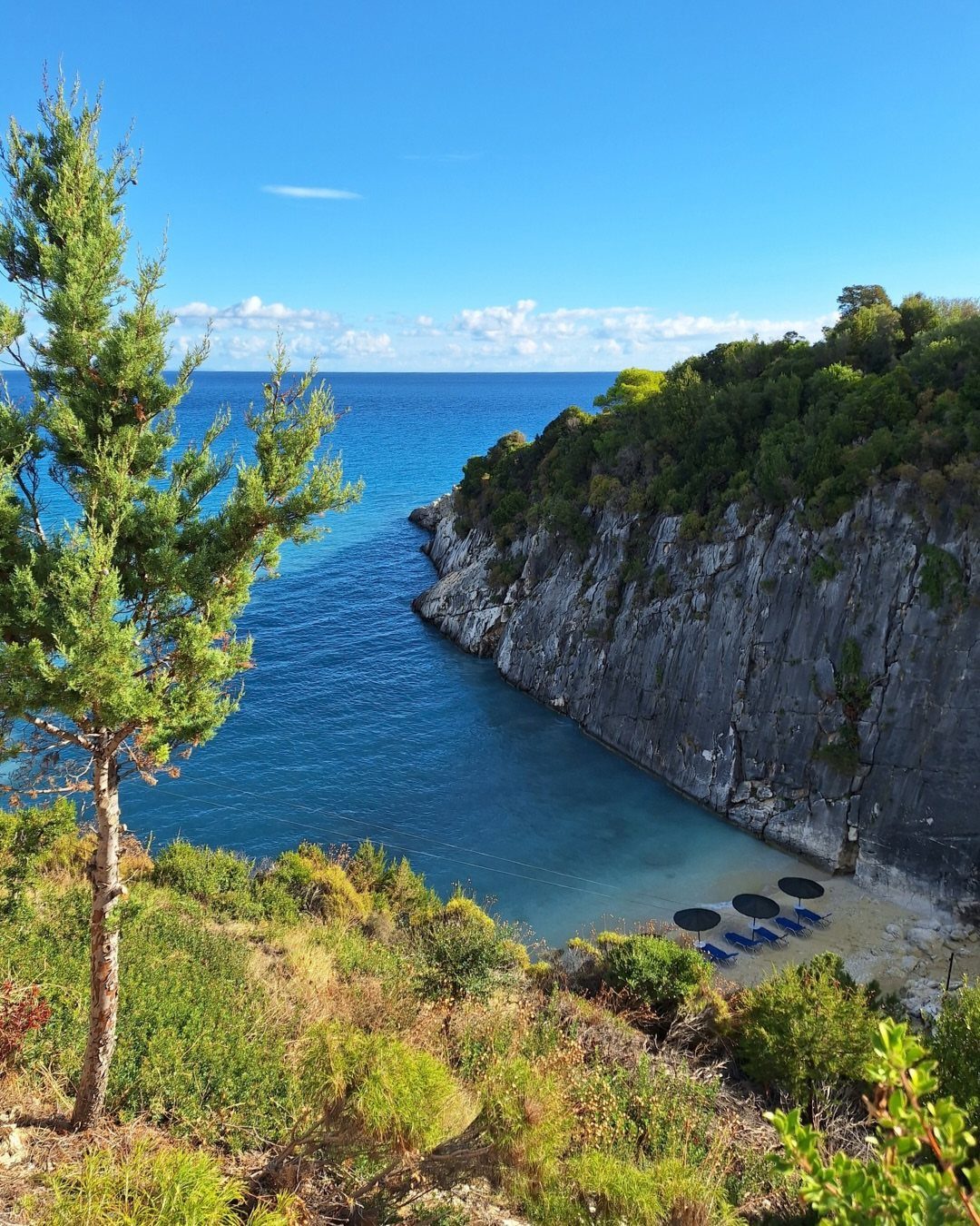 Secluded turquoise cove with a small sandy beach and steep grey cliffs.