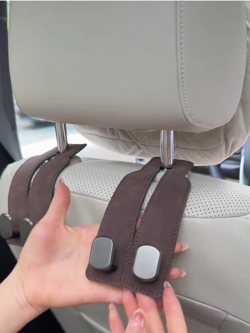 Hands attaching brown leather straps to a grey car seat headrest posts.