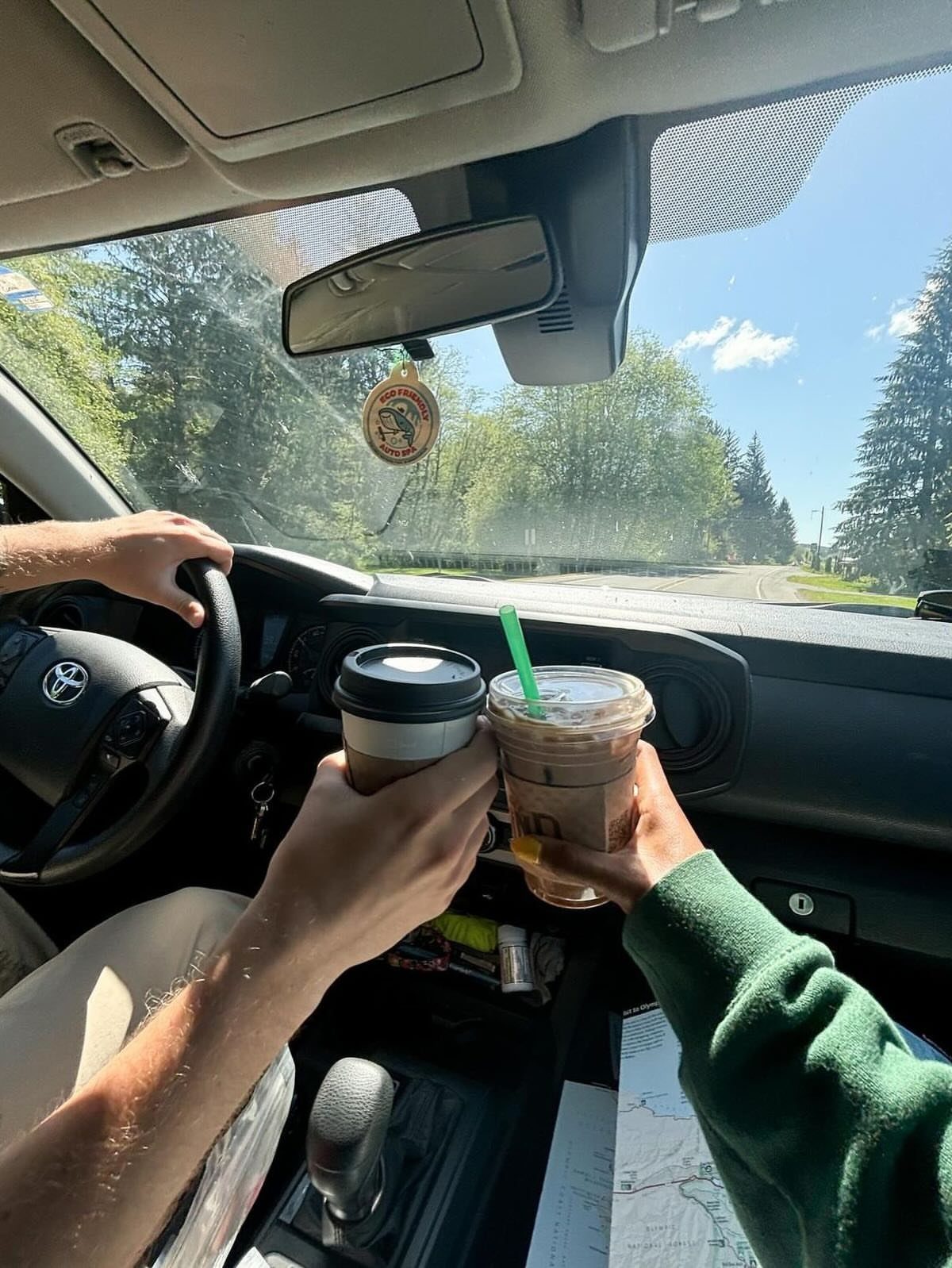 Two people holding coffee drinks inside a car with a map nearby.