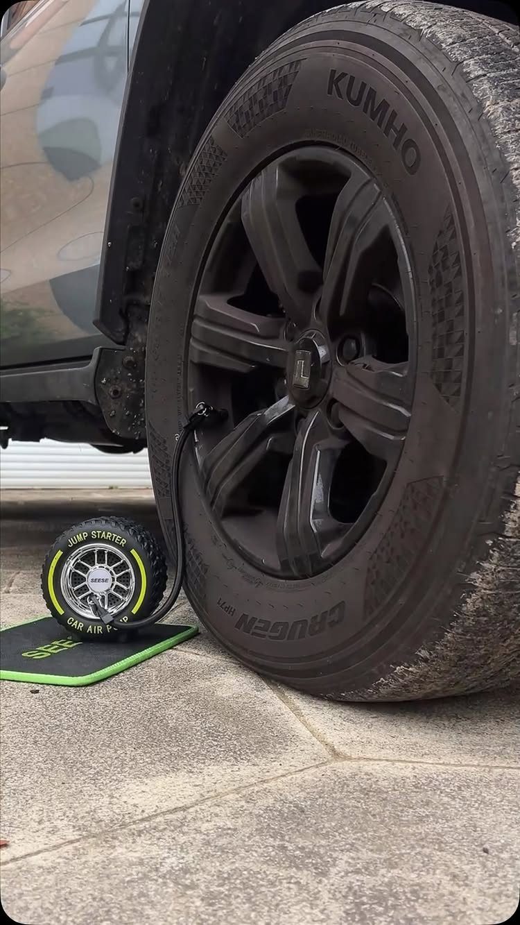 Portable air compressor inflating a black car tire on a concrete driveway