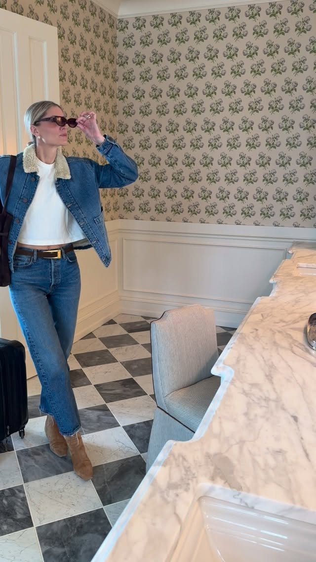 Things to Pack for NYC: 7 Easy Items for Any Trip 7 Woman wearing a denim jacket and boots standing next to a black suitcase.