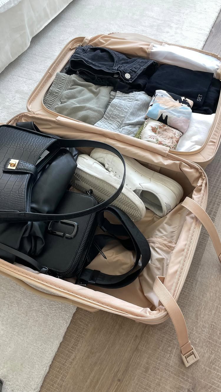 Things to Pack for NYC: 7 Easy Items for Any Trip 6 Open beige suitcase packed with neutral colored clothes, white sneakers, and black handbag.
