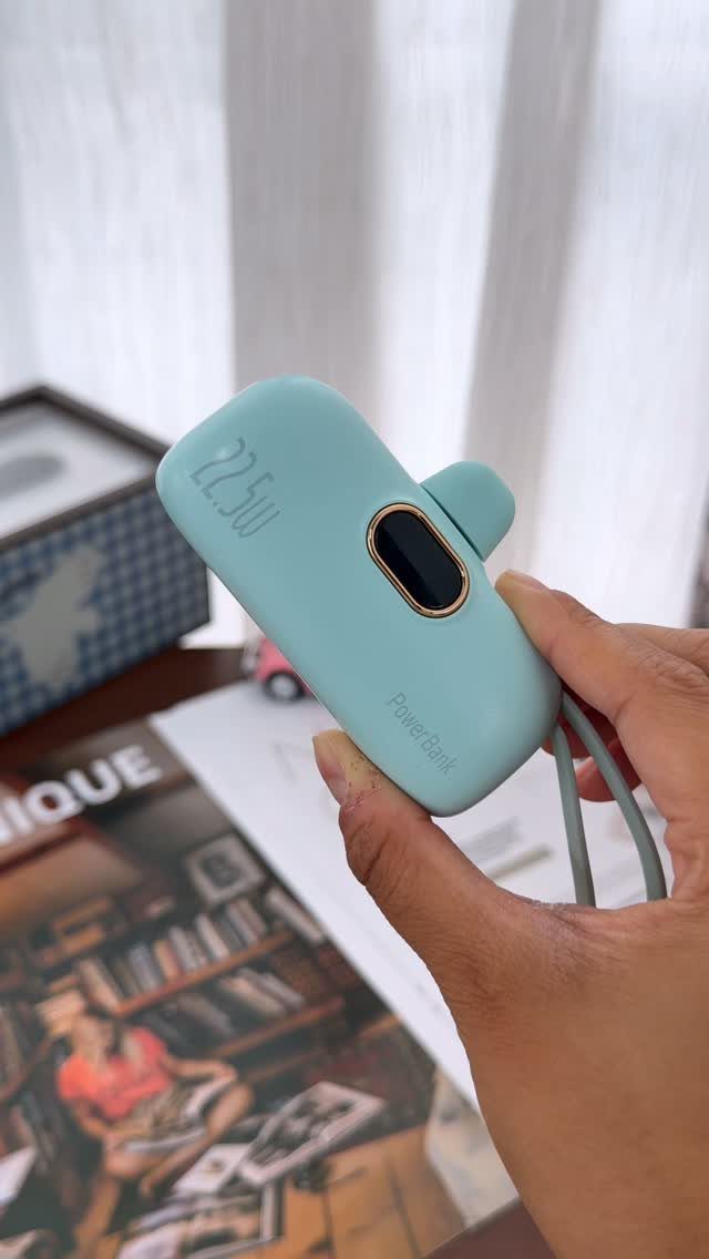 Things to Pack for NYC: 7 Easy Items for Any Trip 1 Light blue portable power bank held in a hand over a blurred background.