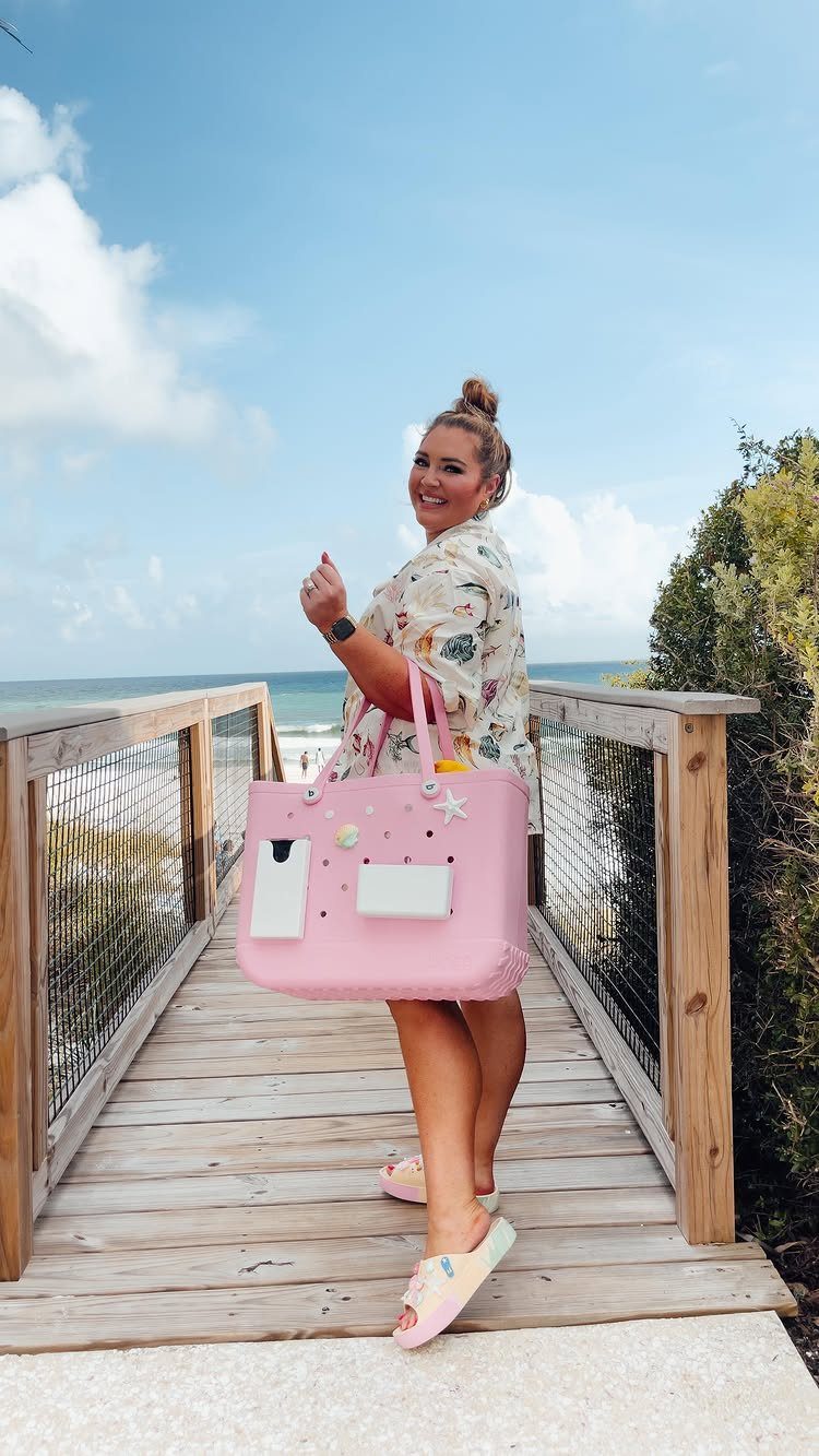 Woman on a wooden boardwalk carrying a large pink neoprene beach tote bag.