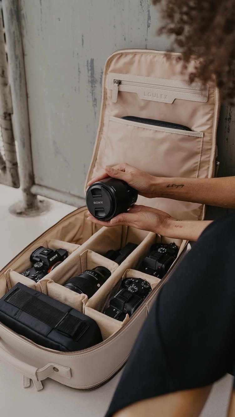 Person organizing black camera lenses and bodies inside a beige padded gear bag.
