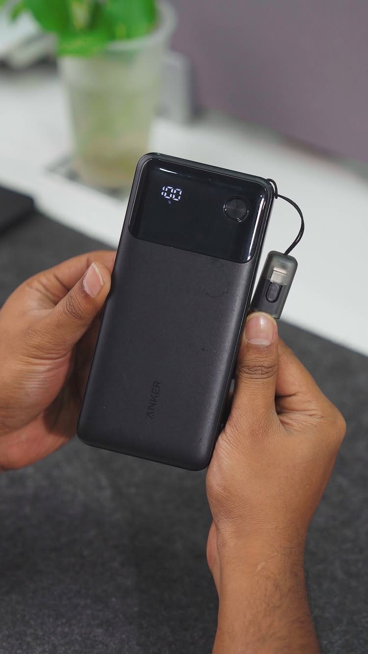 Hands holding a black smartphone being charged by a small portable power bank.