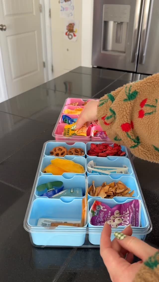Snacks organized in blue and pink divided plastic containers on a black counter