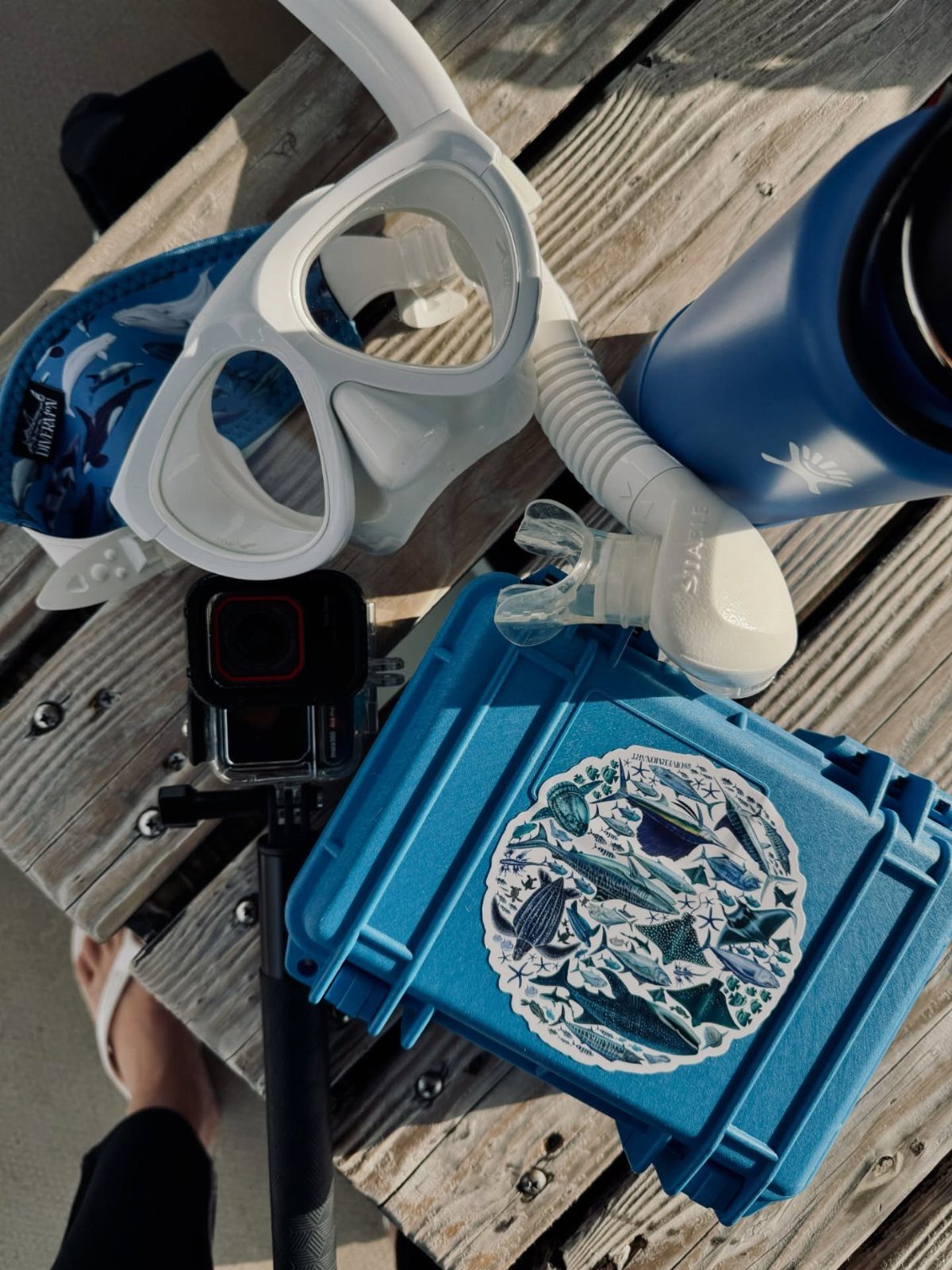 White snorkel mask and tube next to a blue equipment case on wooden decking.