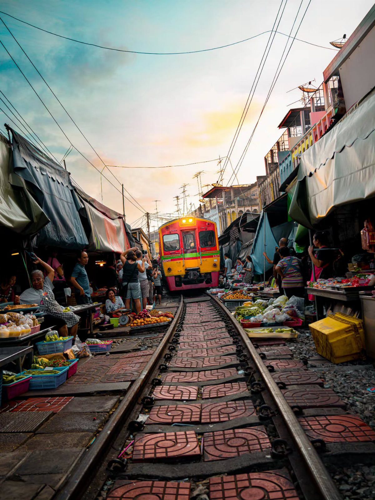 Colorful train passing through a bustling outdoor market along railway tracks in Thailand