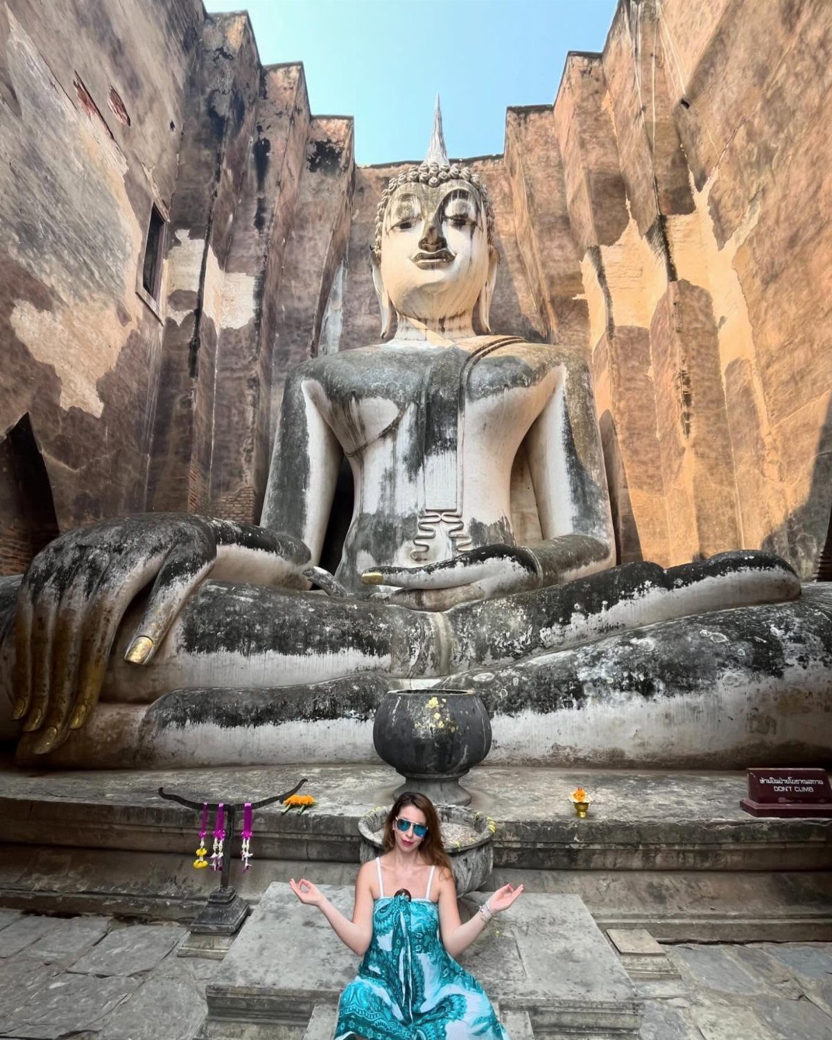 Woman sitting before a giant white Buddha statue in ancient stone ruins