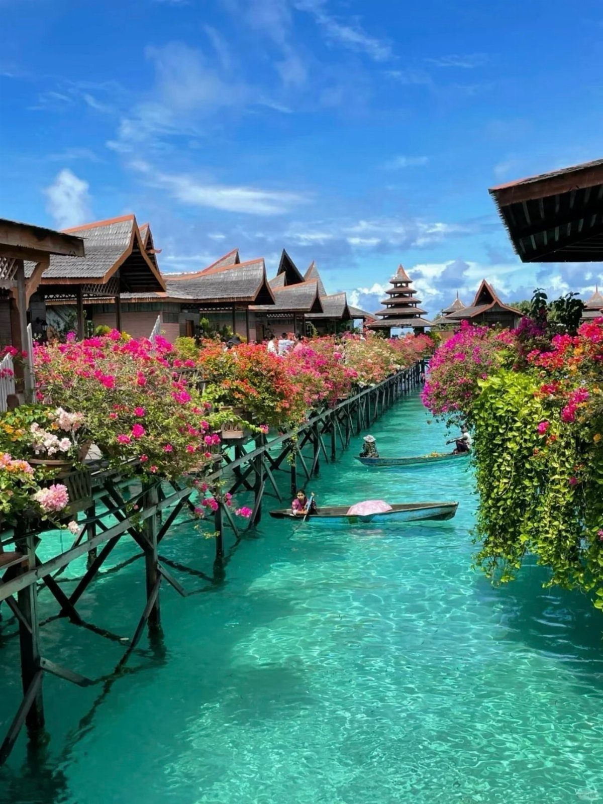 Turquoise canal with traditional Thai wooden houses and bright pink bougainvillea flowers.
