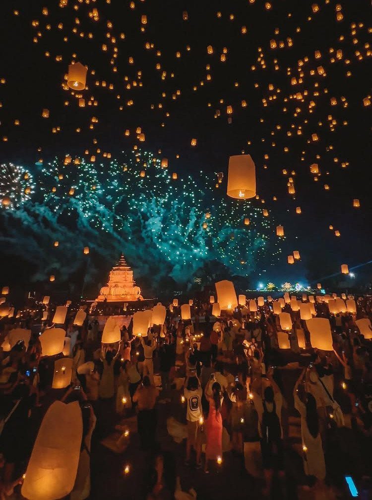 Glowing lanterns floating in the night sky over a crowd and Thai temple.