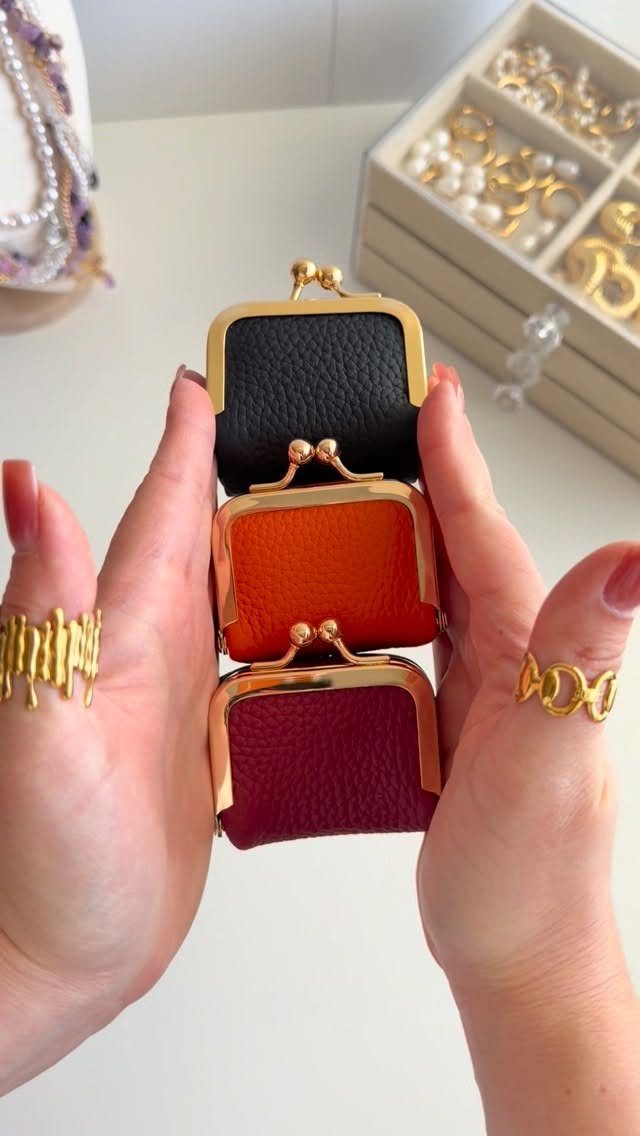 Travel Necessities for Japan: 10 Items Worth Packing 5 Three small leather coin purses in black, orange, and burgundy held by hands.