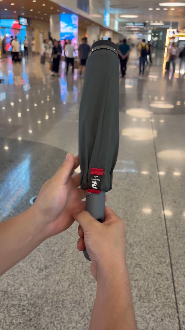 Travel Necessities for Japan: 10 Items Worth Packing 7 Closed grey compact umbrella held by hands in a blurred airport terminal