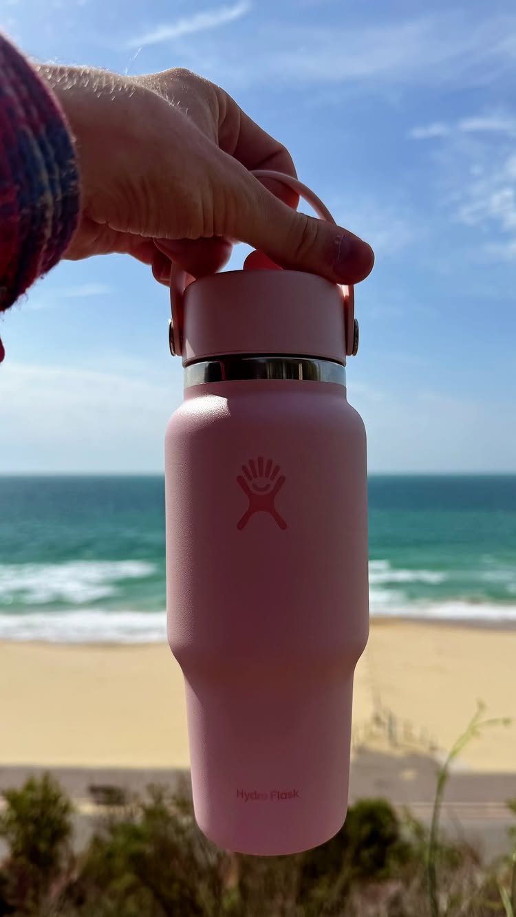 Travel Necessities for Japan: 10 Items Worth Packing 2 Pink reusable water bottle held up against a sunny beach and ocean background.