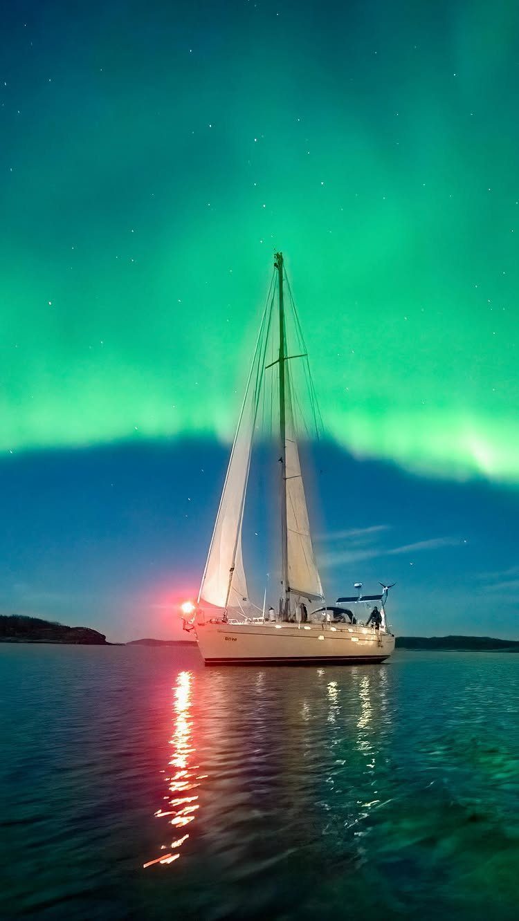 White sailboat on calm water under a bright green aurora borealis night sky