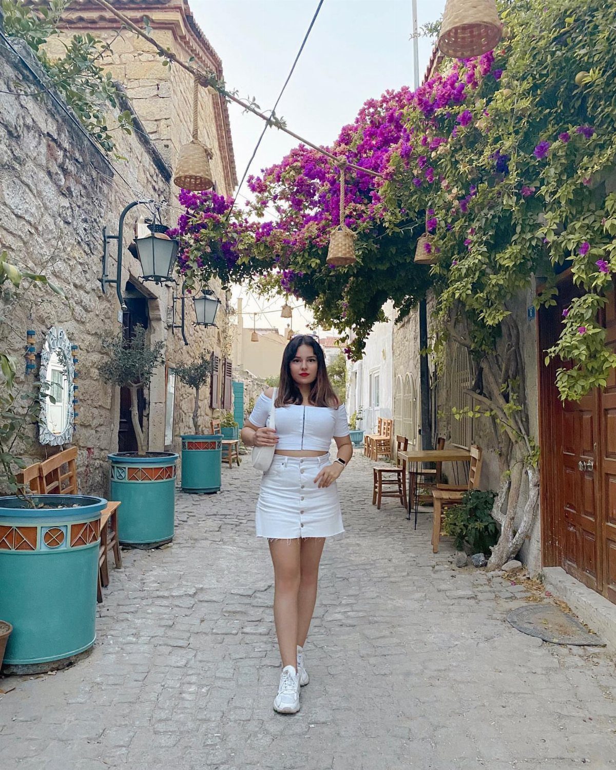 Woman in white outfit standing in a cobblestone street with purple bougainvillea flowers.