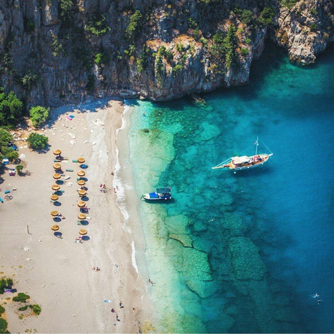 Turquoise water and sandy beach with yellow umbrellas beneath steep rocky cliffs.