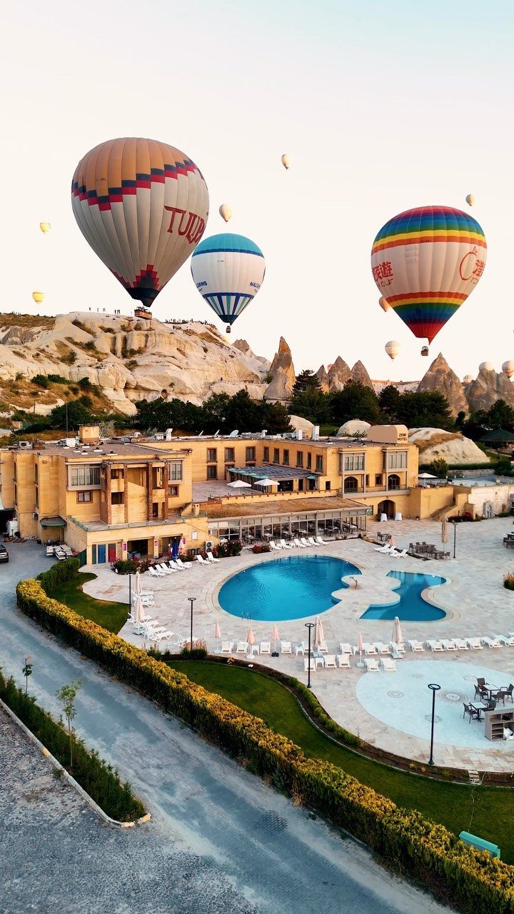 Hot air balloons floating over a hotel pool and Cappadocia rock formations.