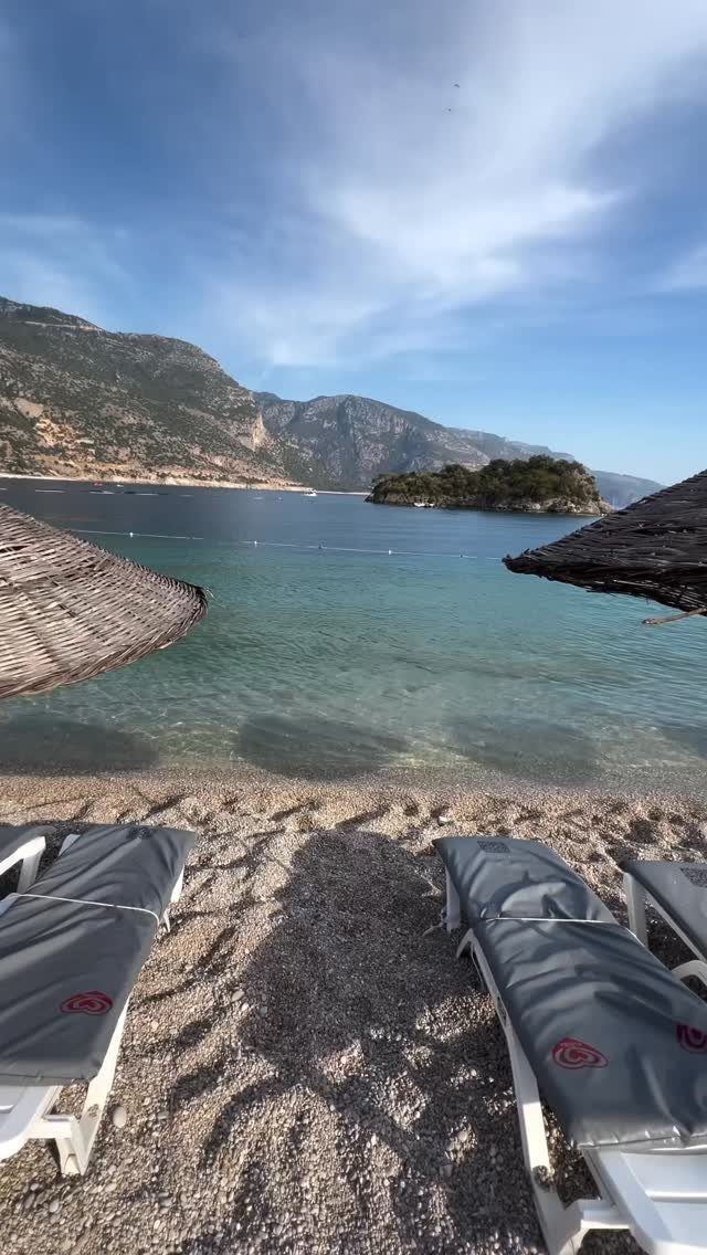 Pebble beach with lounge chairs overlooking turquoise water and distant mountains in Turkey.