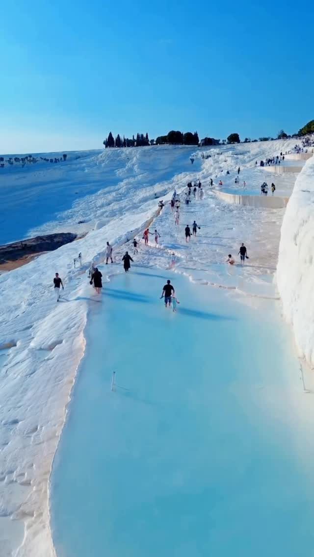 White travertine terraces with bright blue thermal pools and visitors walking through them.