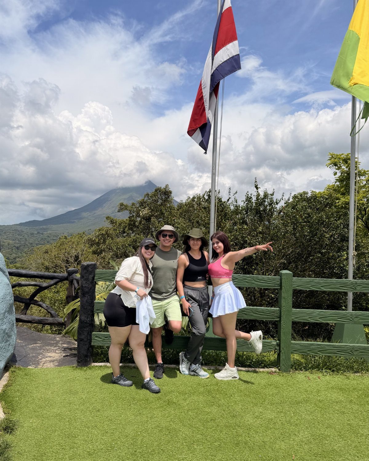 12 Vacation Ideas with Friends, from Cruises to Cancun 4 Four friends posing in front of a Costa Rican flag and rainforest mountains.