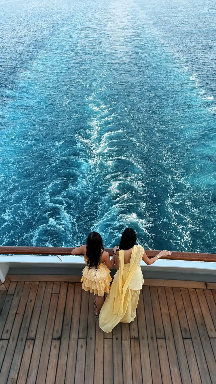 12 Vacation Ideas with Friends, from Cruises to Cancun 1 Two women in yellow dresses looking at the ship's wake from a deck.
