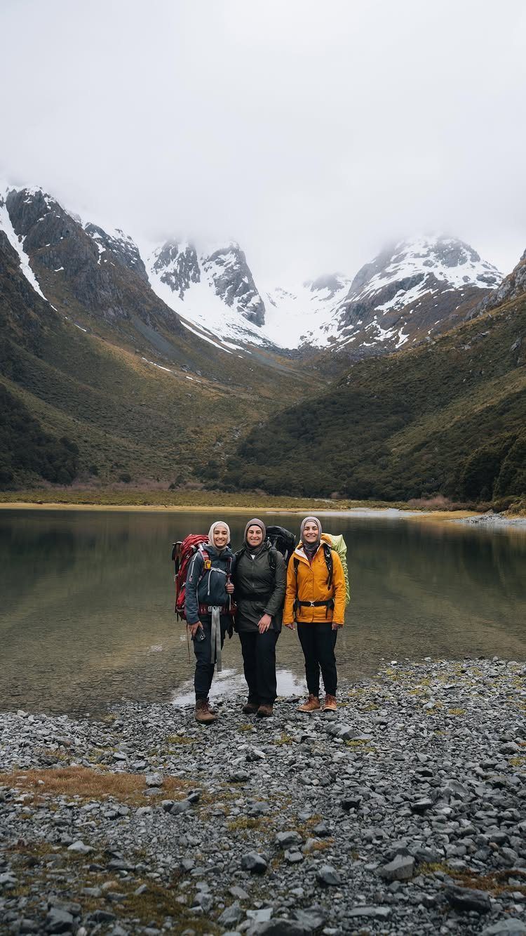 12 Vacation Ideas with Friends, from Cruises to Cancun 9 Three women with hiking backpacks standing by a lake with snowy mountains behind.