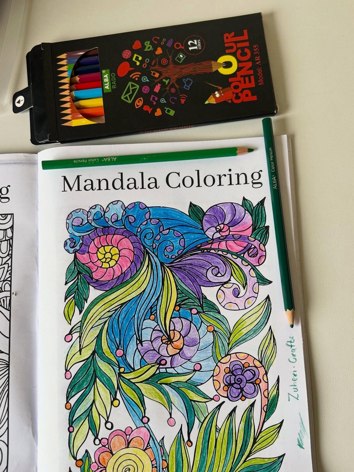 9 Ideas for What to Do on the Plane Besides Scrolling 3 Colored mandala coloring page with a green pencil and a box of pencils.