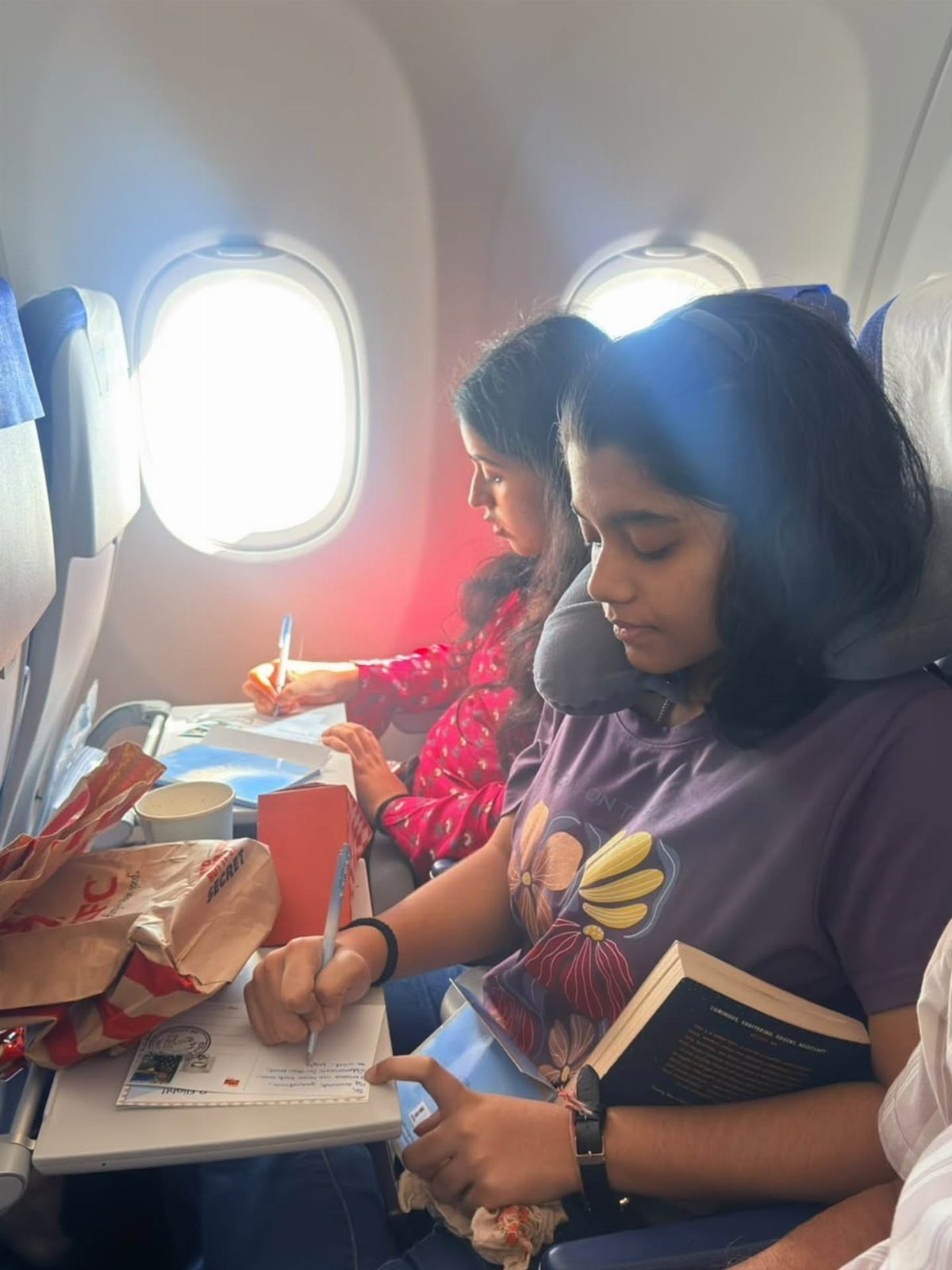 9 Ideas for What to Do on the Plane Besides Scrolling 9 Two women writing on papers while sitting in airplane seats during a flight.