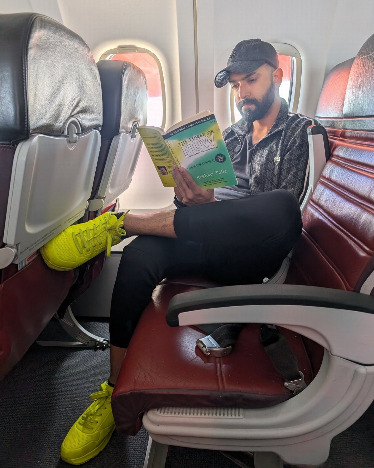 9 Ideas for What to Do on the Plane Besides Scrolling 1 Man in yellow sneakers reading a book while sitting in an airplane seat.