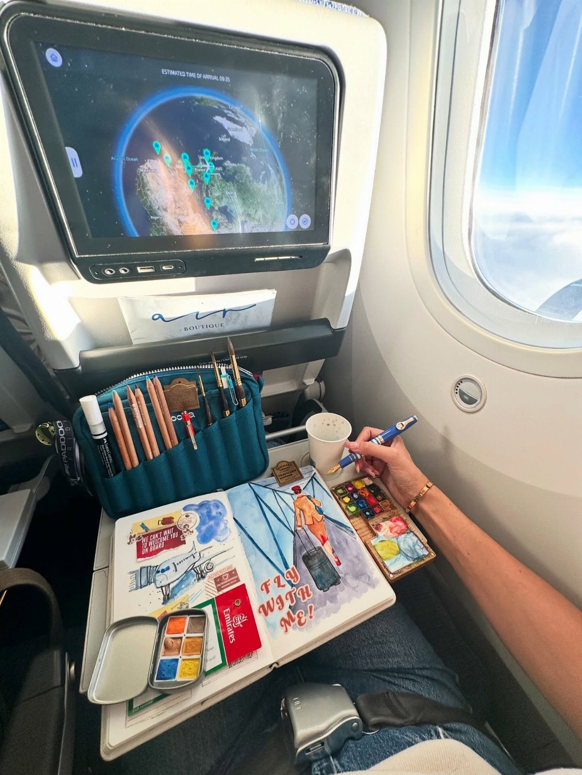 9 Ideas for What to Do on the Plane Besides Scrolling 7 Person painting in a sketchbook on an airplane tray table during a flight