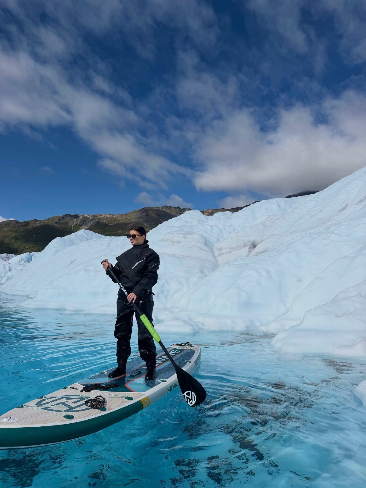 Person on a paddleboard in blue water next to massive white glaciers