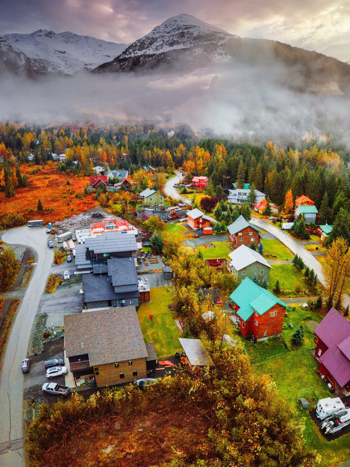Colorful village houses surrounded by autumn foliage with a foggy mountain peak behind.