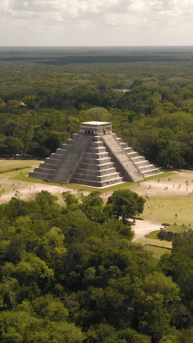 Large stone stepped Mayan pyramid surrounded by lush green jungle and grassy plains.
