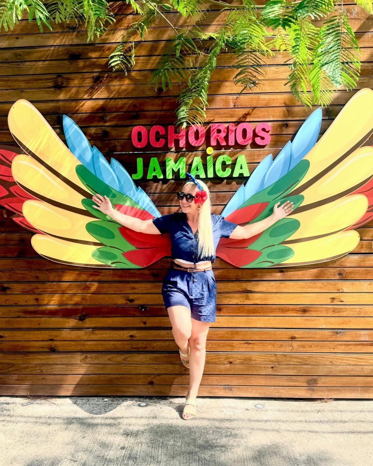 Woman posing in front of colorful wings and Ocho Rios Jamaica sign on wood wall