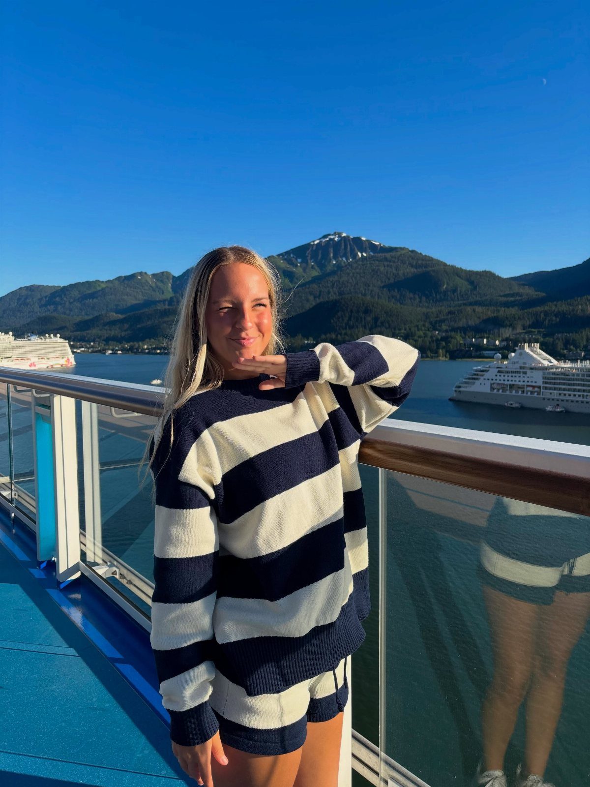 Woman in striped outfit posing on a cruise ship deck with mountains behind.