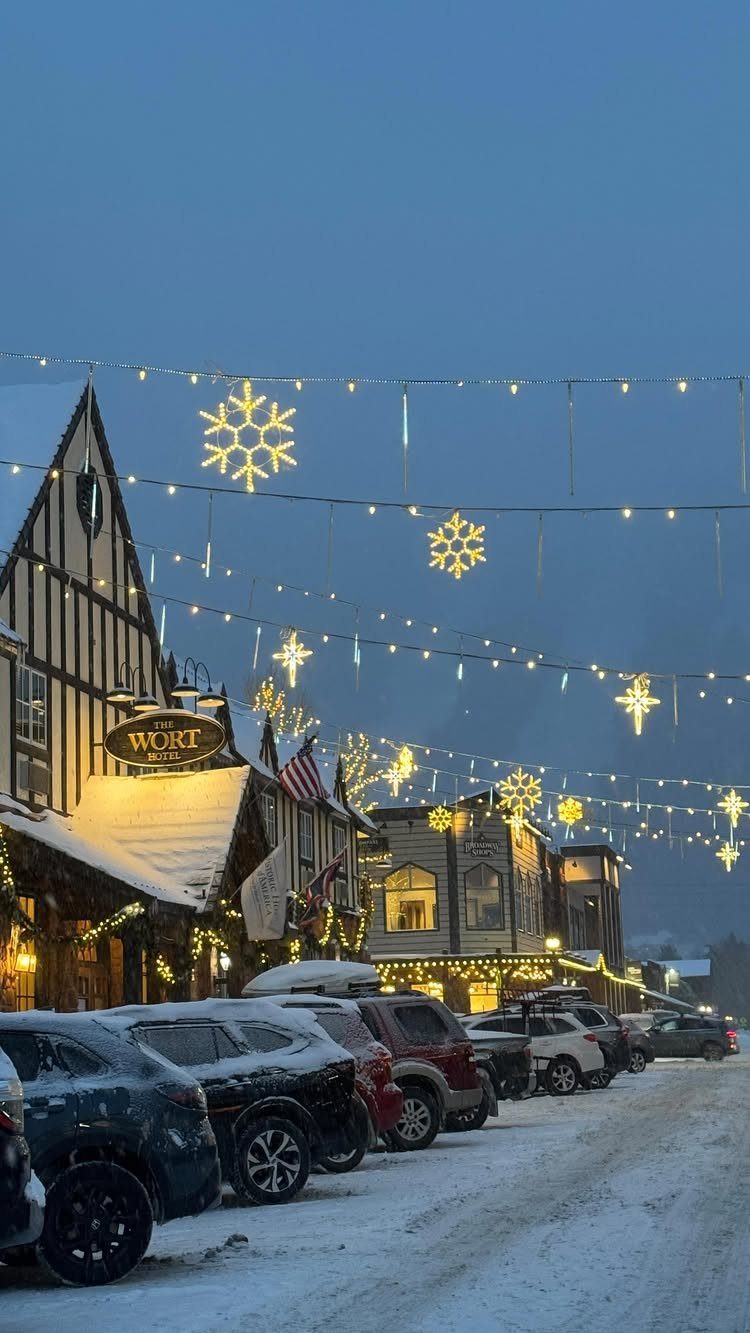 Snowy street at dusk with Tudor buildings and glowing snowflake string lights.