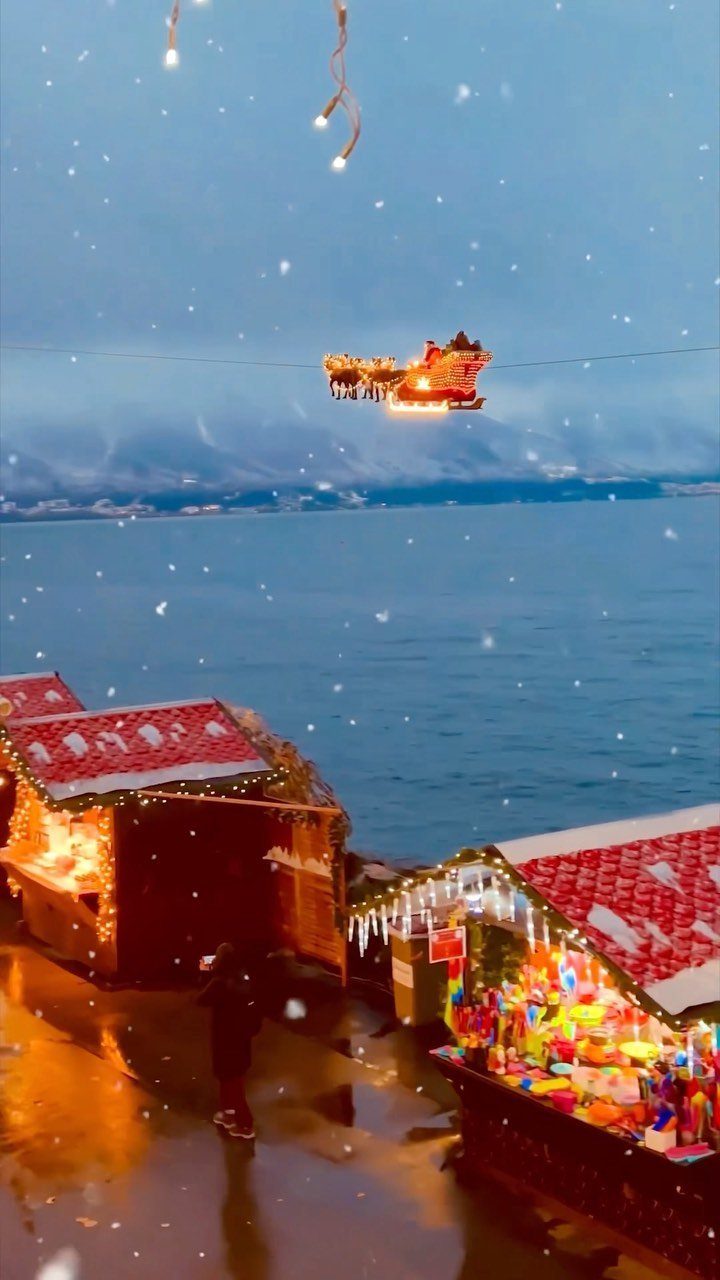 Festive market stalls and a glowing flying Santa sleigh by a winter lake