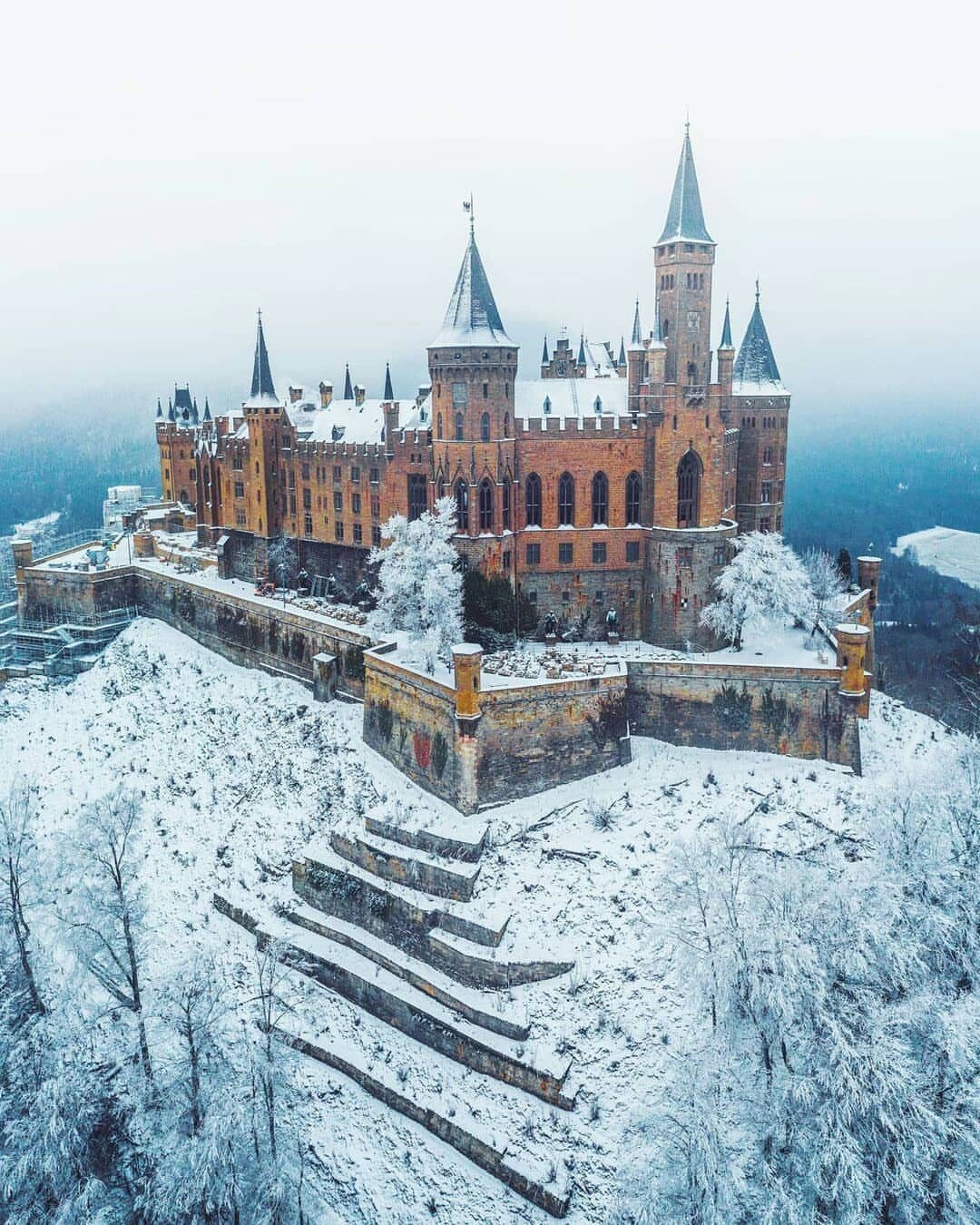 Ornate stone castle with spires sitting on a snowy hill among frosted trees