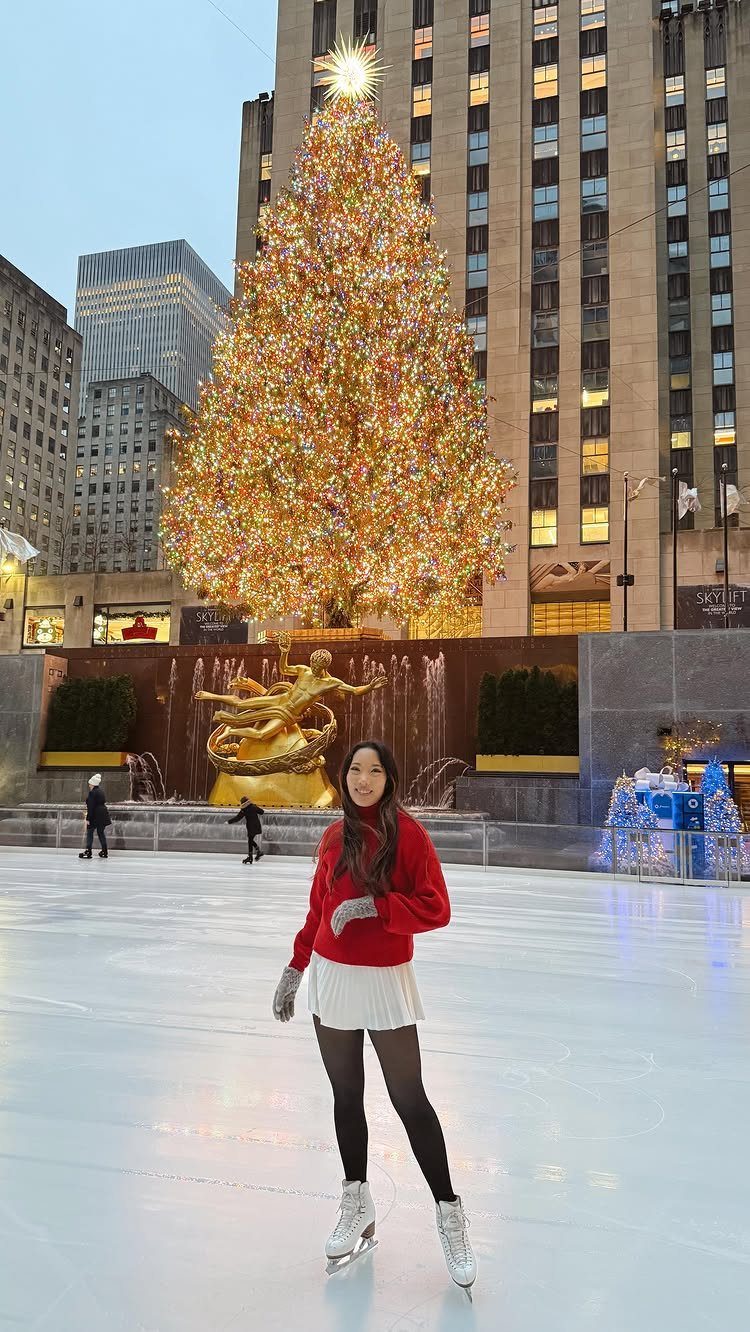 Woman in red sweater ice skating in front of Rockefeller Center Christmas tree