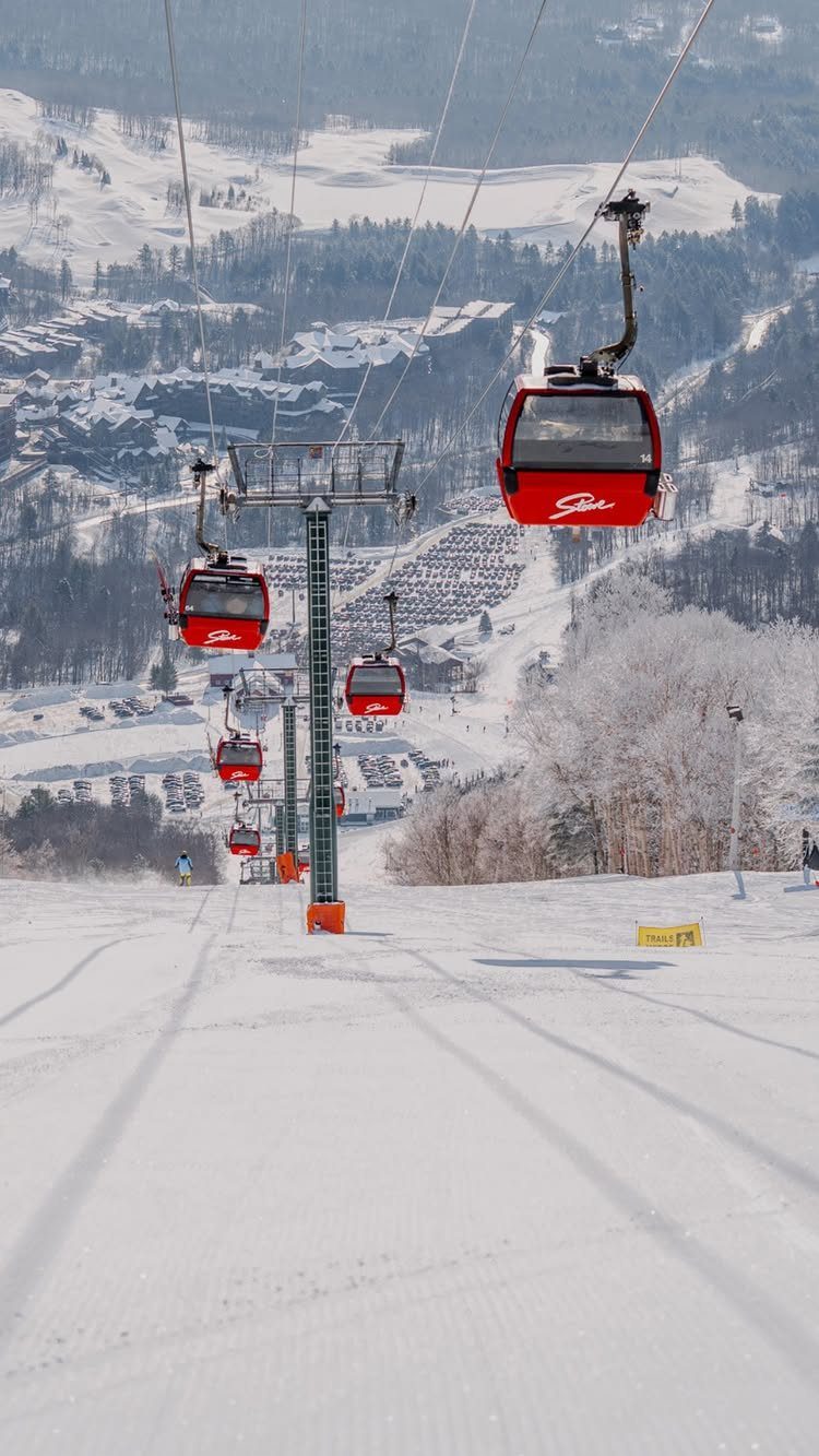 Red gondola lifts ascending a snowy mountain slope toward a distant valley.