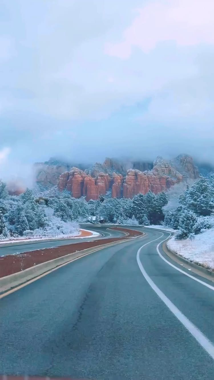 Winding road leading toward red rock formations covered in winter snow
