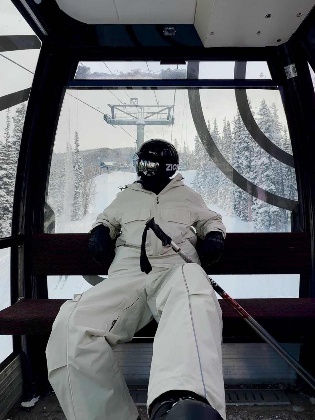 Skier in white gear sitting in a gondola overlooking snowy mountain slopes