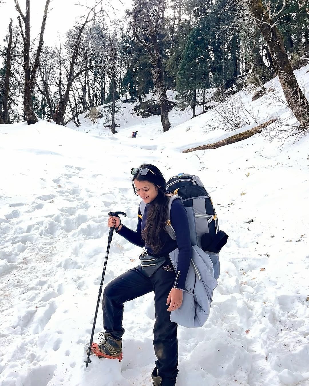 Woman with hiking gear and backpack standing in a snowy forest landscape